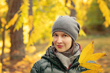 Portrait of beautiful smiling girl in gray hat holding yellow autumn leaves