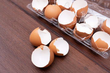 Close up of broken organic raw chicken eggs shell in plastic egg case with three broken eggs shell on brown wooden floor background