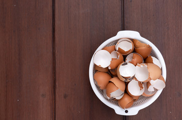 Top view of broken organic raw chicken eggs shell in white plastic basket on brown wooden floor background with copy space