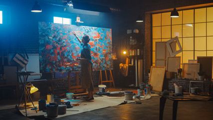 Talented Female Artist Works on Abstract Oil Painting, with Broad Strokes of Paint Brush She Creates Modern Masterpiece. Dark and Messy Creative Studio where Large Canvas Stands on Easel Illuminated 