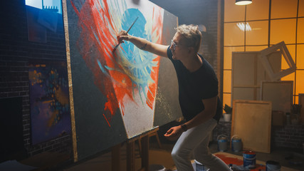 Talented Artist Working on Abstract Painting, Uses Paint Brush To Create Daringly Emotional Modern Picture. Dark Creative Studio Large Canvas Stands on Easel Illuminated.