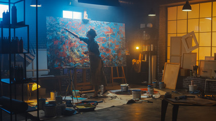 Talented Female Artist Works on Abstract Oil Painting, Using Paint Brush She Creates Modern Masterpiece. Dark and Messy Creative Studio where Large Canvas Stands on Easel Illuminated