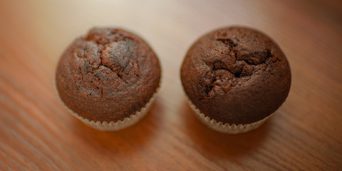 two chocolate muffins on the brown wooden table.