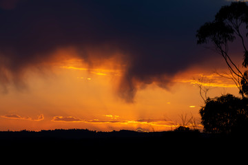 A vivid orange sunset in The Blue Mountains in Australia with a valley and trees in the foreground.