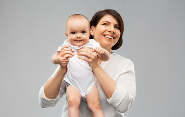 family, child and parenthood concept - happy smiling middle-aged mother holding little baby daughter over grey background