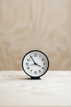 analog alarm clock on wood table with plywood backdrop