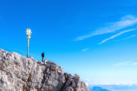 A man traveller stand and relaxing on the peak mountain and looking on blue sky and clouds at German Alps Zugspitze.Happy Vacation holiday in beautiful outdoor scene landscape.Travel Freedom concept.
