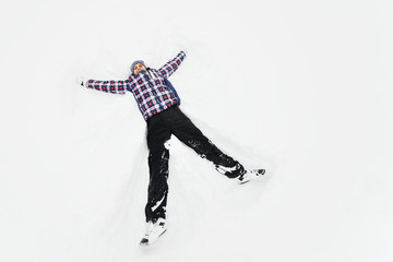 Fototapeta premium a young man in a plaid outerwear or jacket lies on the snow and makes the figure of an angel. Winter fun