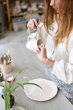 Portrait of female potter painting on jug in pottery workshop