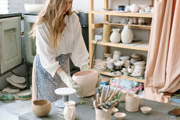 Female artisan standing in her creative ceramic workshop removing newly glazed pieces of pottery from a kiln