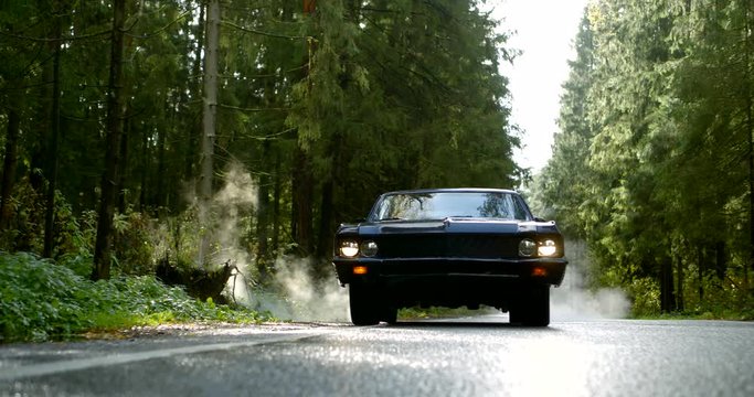 old classic car is moving on countryside road in forest in daytime, frontal view from ground