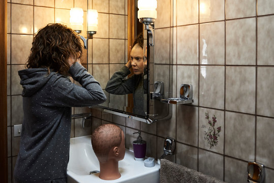 Woman removing peruke bathroom mirror.