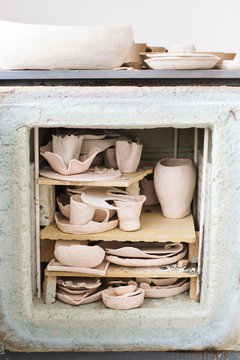 Female artisan standing in her creative ceramic workshop removing newly glazed pieces of pottery from a kiln