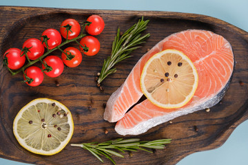 Raw, fresh salmon steak on a wooden board with lemon, rosemary and cherry tomatoes. Raw salmon, red fish. Cooking salmon, seafood. Healthy eating concept. Salmon and spices