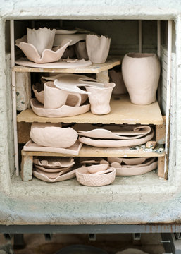 Female artisan standing in her creative ceramic workshop removing newly glazed pieces of pottery from a kiln