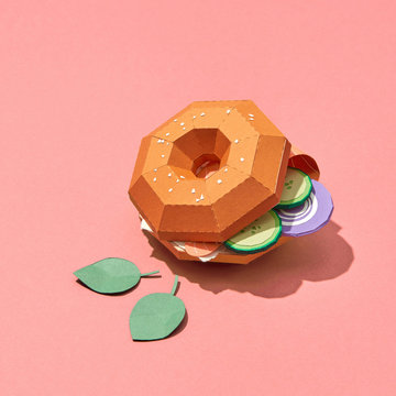 Paper bun, handcraft slices of onion, meat, cucumber cheese and spinach leaves on a coral background with copy space. Fast food. Flat lay