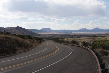 The top of a winding country road on a clear day with a view of mountains