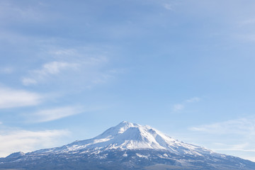 The snow-covered peak of Mount Shasta on a blue sky day
