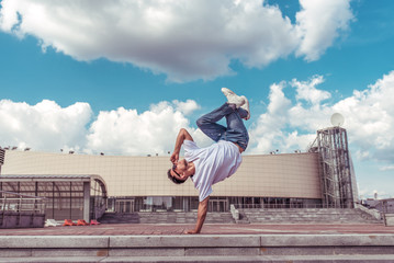 Male athlete, standing on one arm jump, summer city, hip hop style, break dancer. Cloud building background. Active youth lifestyle, modern fashionable, street dancer. Fitness t-shirt glasses jeans.