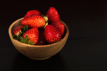 Fresh red strawberries in a wooden bowl on dark wooden background