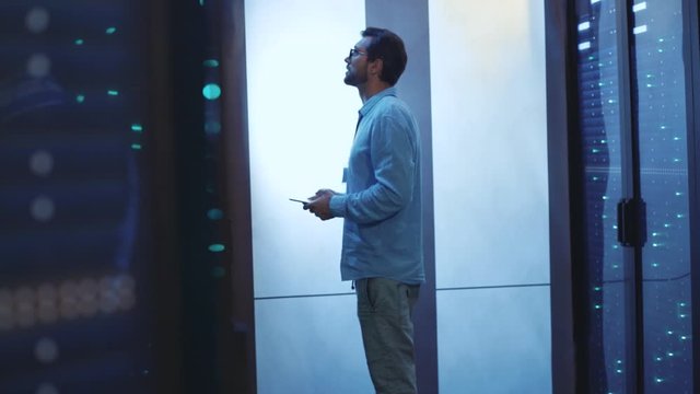 IT administrator with digital tablet examining working system of rack server computers. Male specialist working in modern data network cyber security center.