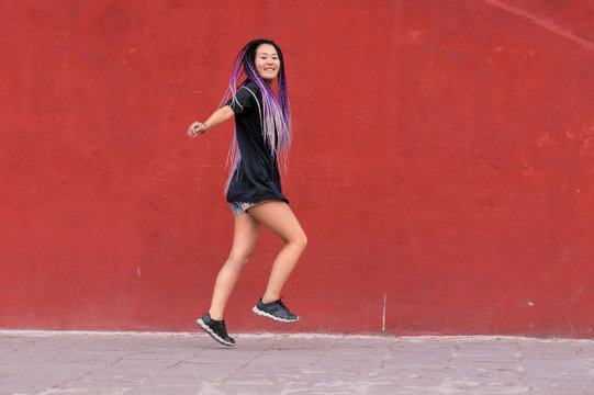 Young woman with purple rasta braids skipping
