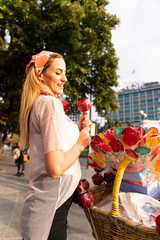 Fototapeta premium Girl holding a lollipop. Beautiful happy blond girl in the street. Young woman eating a piece of candy. 