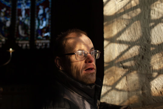 Portrait of a middle aged man with Down's syndrome standing by a window in an old church.