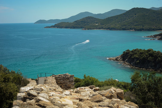 View of the boat and the sea through the forest. Blue sea and motorboat. The Sea Bay at the historic Greek city of Stagira