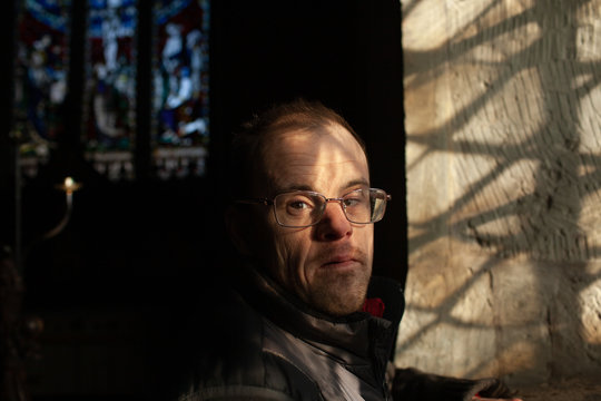 Portrait of a middle aged man with Down's syndrome standing by a window in an old church.