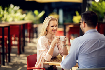 Happy woman drinking coffee and talking to her boyfriend in a cafe.