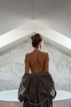 Nude woman in bathrobe on white tile background