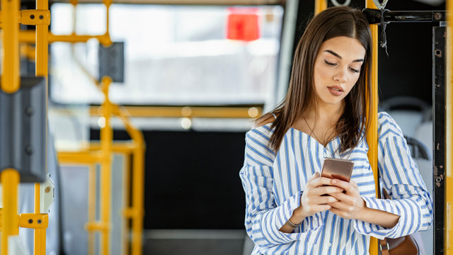 Young woman traveling by bus and using smart phone. Woman with phone at the public transport. Woman with phone at the public transport. Sweet girl using phone while standing in a bus.