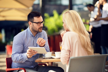 Couple using touchpad and talking while sitting in a cafe.