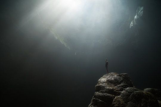 Girl stands under the rays of light in a deep cave Jomblang Cave. Java, Indonesia