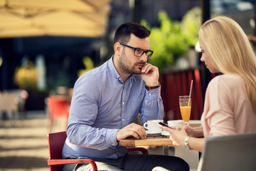 Displeased man looking at his girlfriend who is text messaging on mobile phone in a cafe.