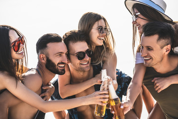 The six friends clink bottles of beer outdoor