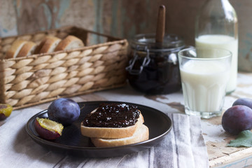 Bread toast with plum jam, served with milk and plums on a wooden background. Rustic style.