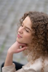 Fototapeta premium Profile view of young woman with curly hair resting her head on her hand