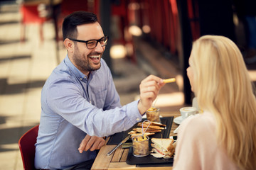 Happy man feeding his girlfriend with French fries in a restaurant.