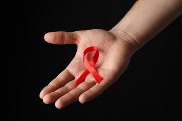 Hand and red awareness ribbon against black background, space for text - obrazy, fototapety, plakaty
