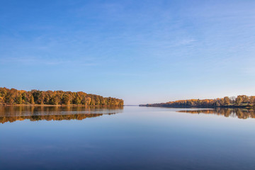 Fototapeta premium View looking down calm water at dawn with autumn trees and reflections nobody