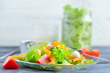 Leaf lettuce salad with tomatoes and mozzarella on a glass plate.