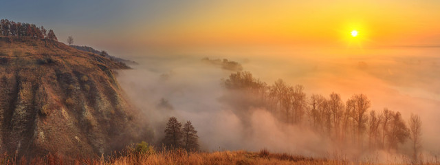 Naklejka na ściany i meble Autumn sunrise landscape, panorama, banner - view of a river valley covered with fog in the light of the sunrays, the northeast of Ukraine