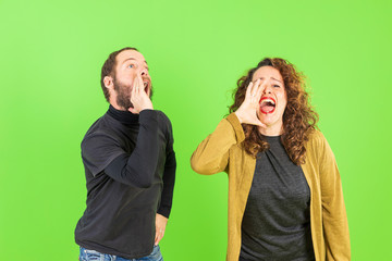 Young beautiful couple over green background, mad, shouting and yelling with aggressive expression.Frustration and crazy concept.