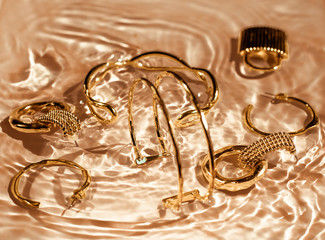 Golden bracelets, earrings, rings, jewelery on gold water background, luxury glamour and holiday...