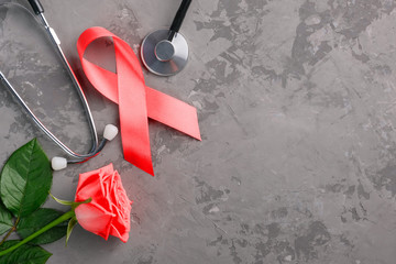 red ribbon, stethoscope and rose on a concrete background. 1 December World AIDS Day, HIV illness campaign.