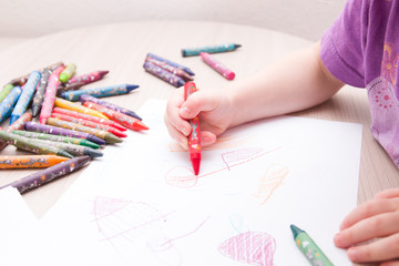 child draws in red colored chalk on paper