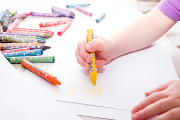 child draws the sun in crayons on paper