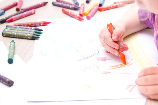 child draws with crayons on paper